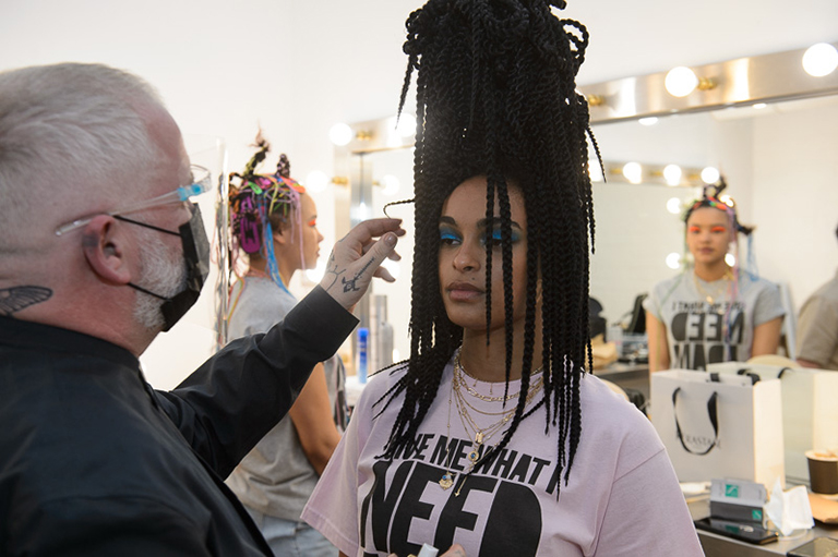 Adam Reed preparing a hair model with long braids in a towering bun backstage at Creative HEAD Magazine's Salon Smart Live 2021